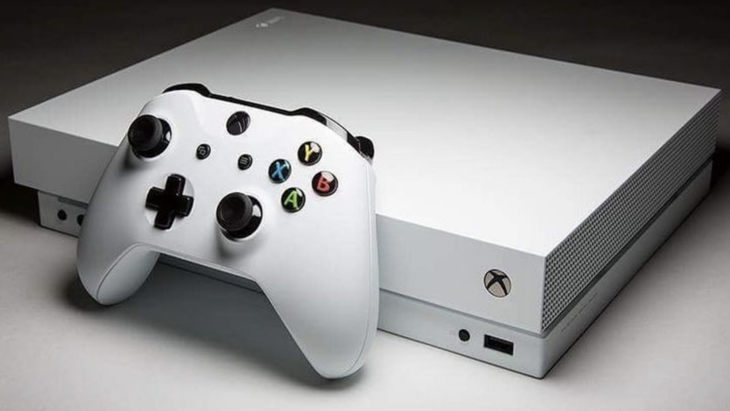 A white Xbox gaming console with a matching wireless controller resting on top. This sleek consoles features a power button, USB port, and vent on the front side.