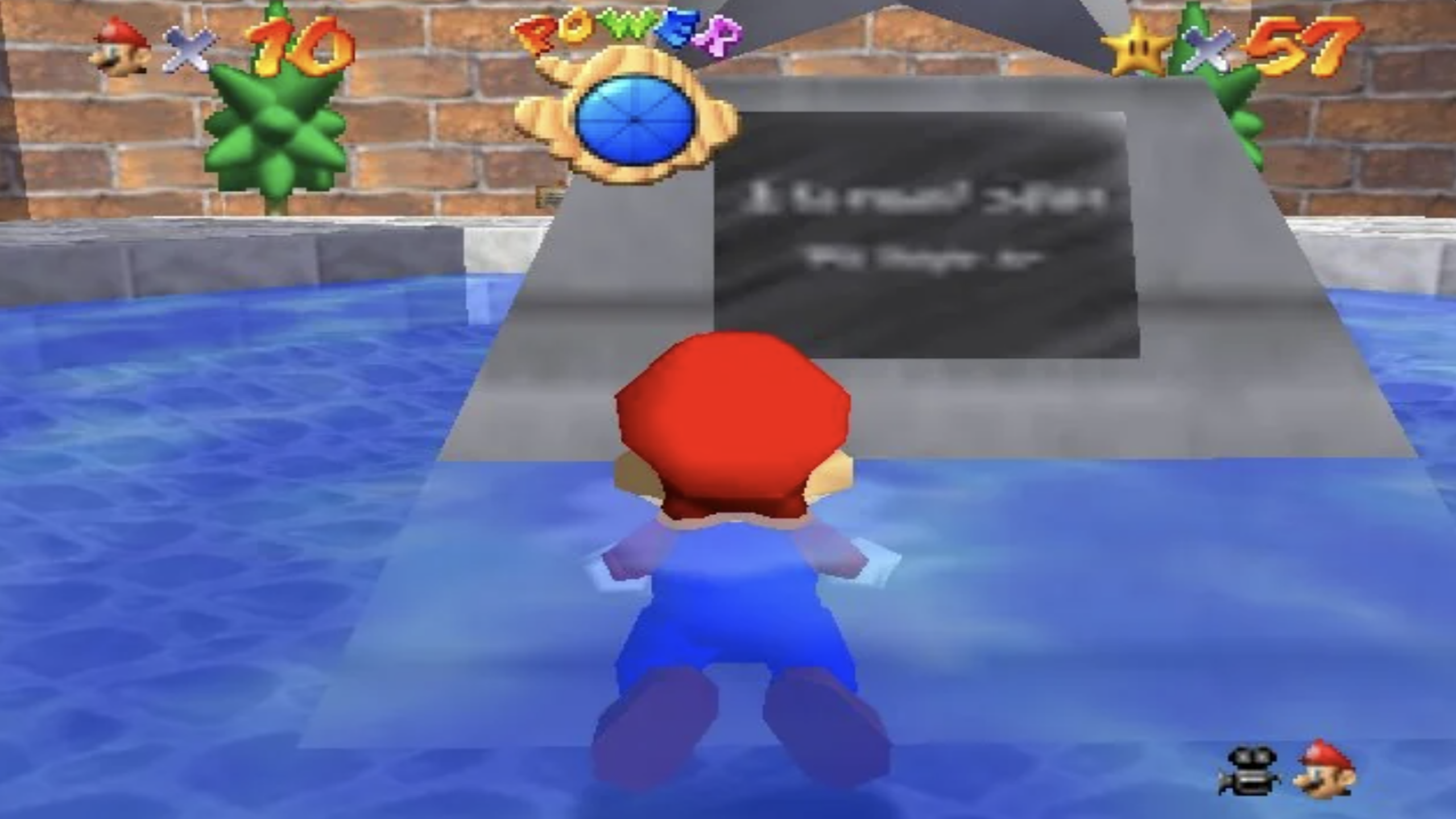 Mario stands in shallow water facing a blurry plaque on a gray monument in Super Mario 64, with health, lives, and star counters shown on the screen—a classic moment from this iconic video game.