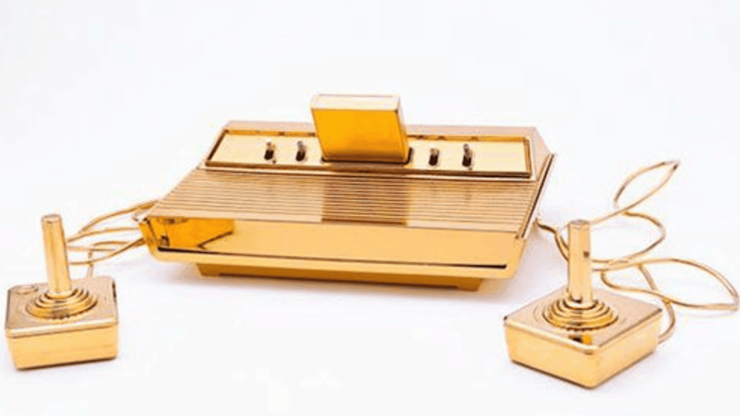 A gold-plated vintage video game console with two matching gold joystick controllers and a cartridge inserted, all on a white background.
