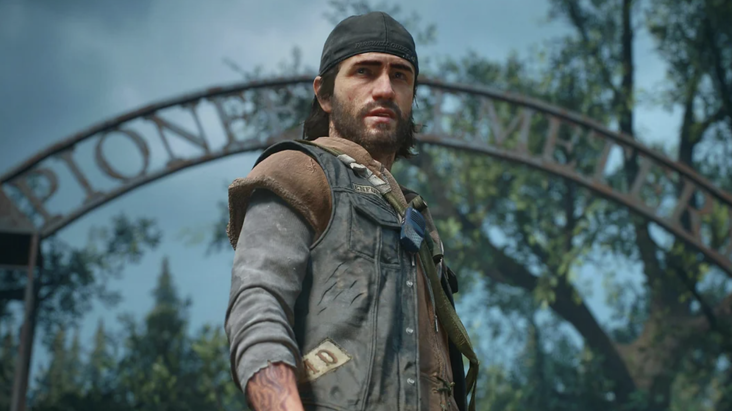 A rugged man in a backward cap and vest stands outdoors, looking into the distance. Behind him, a metal archway says "PIONEER CEMETERY" and trees fill the background under a blue sky, evoking the spirit of adventure and the camaraderie often found in outdoor physical games.