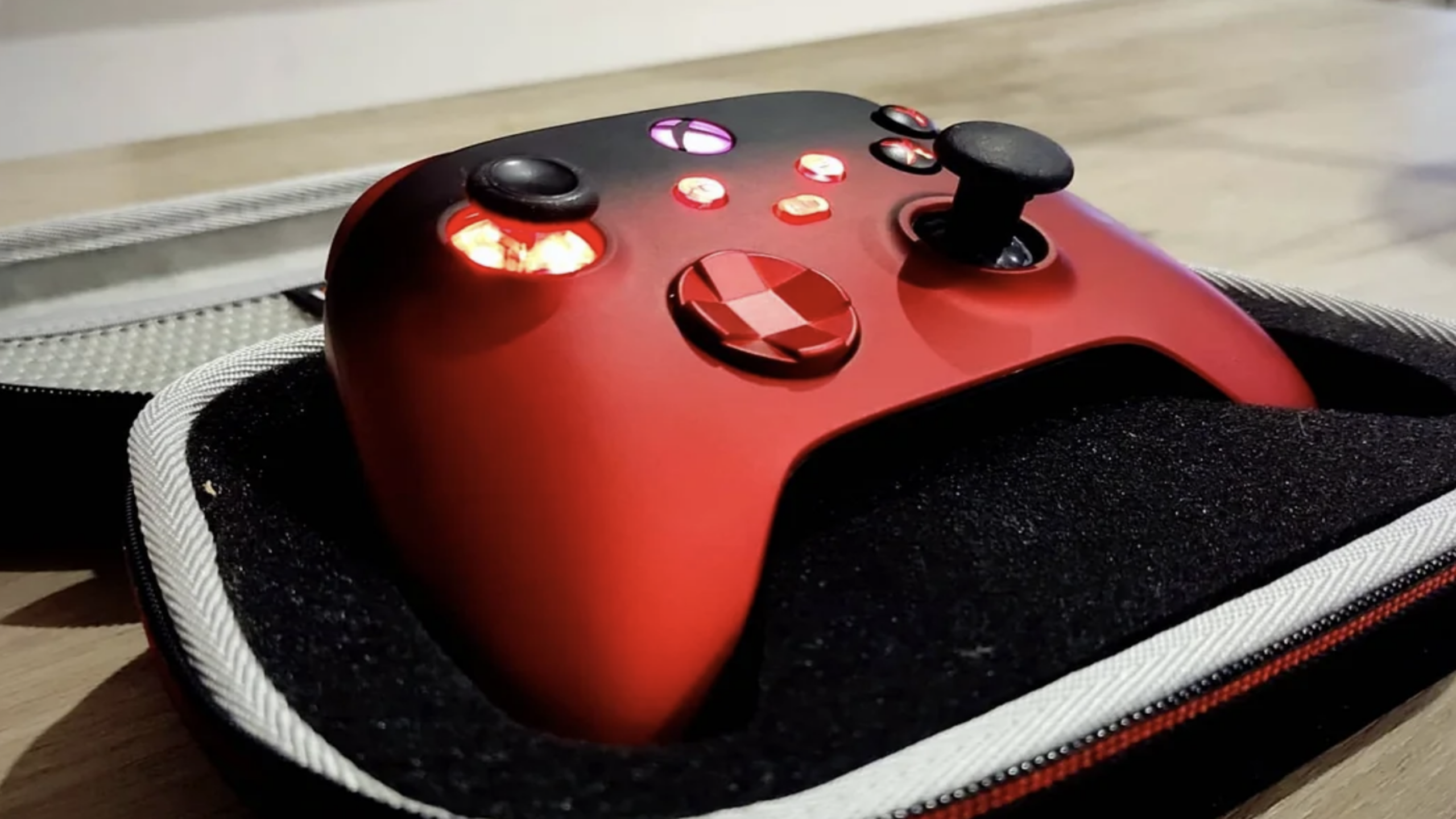 A red and black Xbox controller with glowing buttons, the epitome of expensive gaming, rests in a foam case on a wooden table.