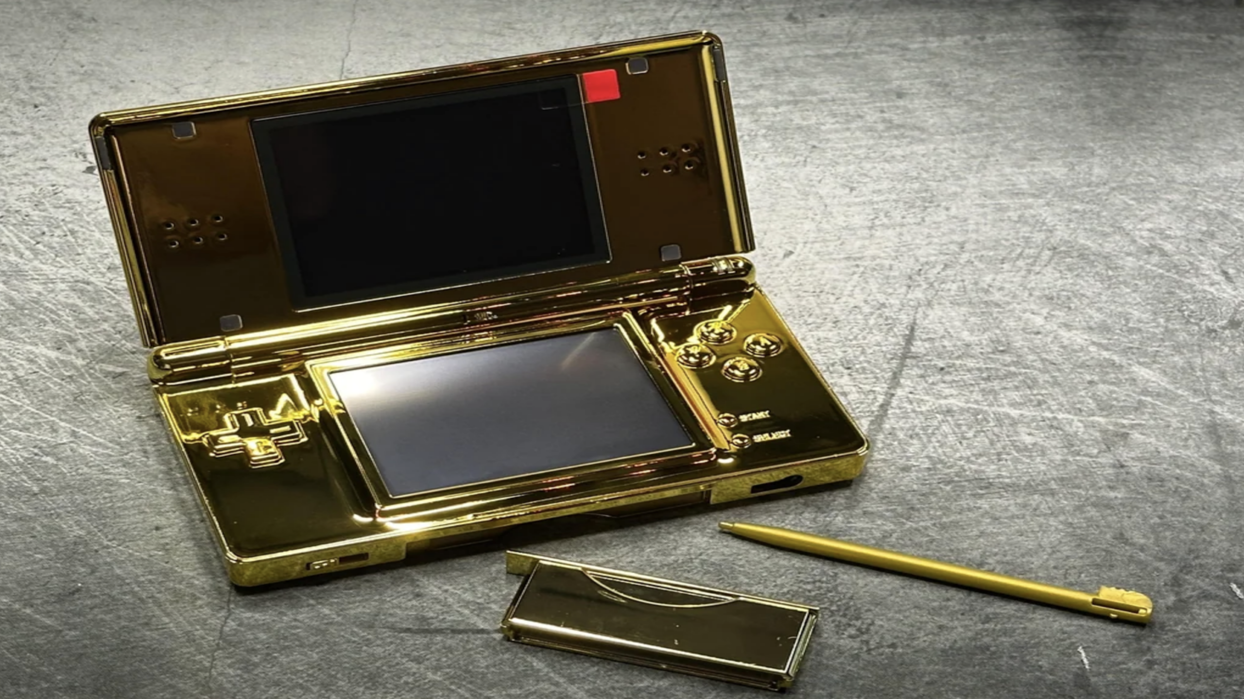 A gold-colored Nintendo DS handheld console, one of the most iconic gaming consoles, is displayed with its stylus and cartridge on a metallic surface.
