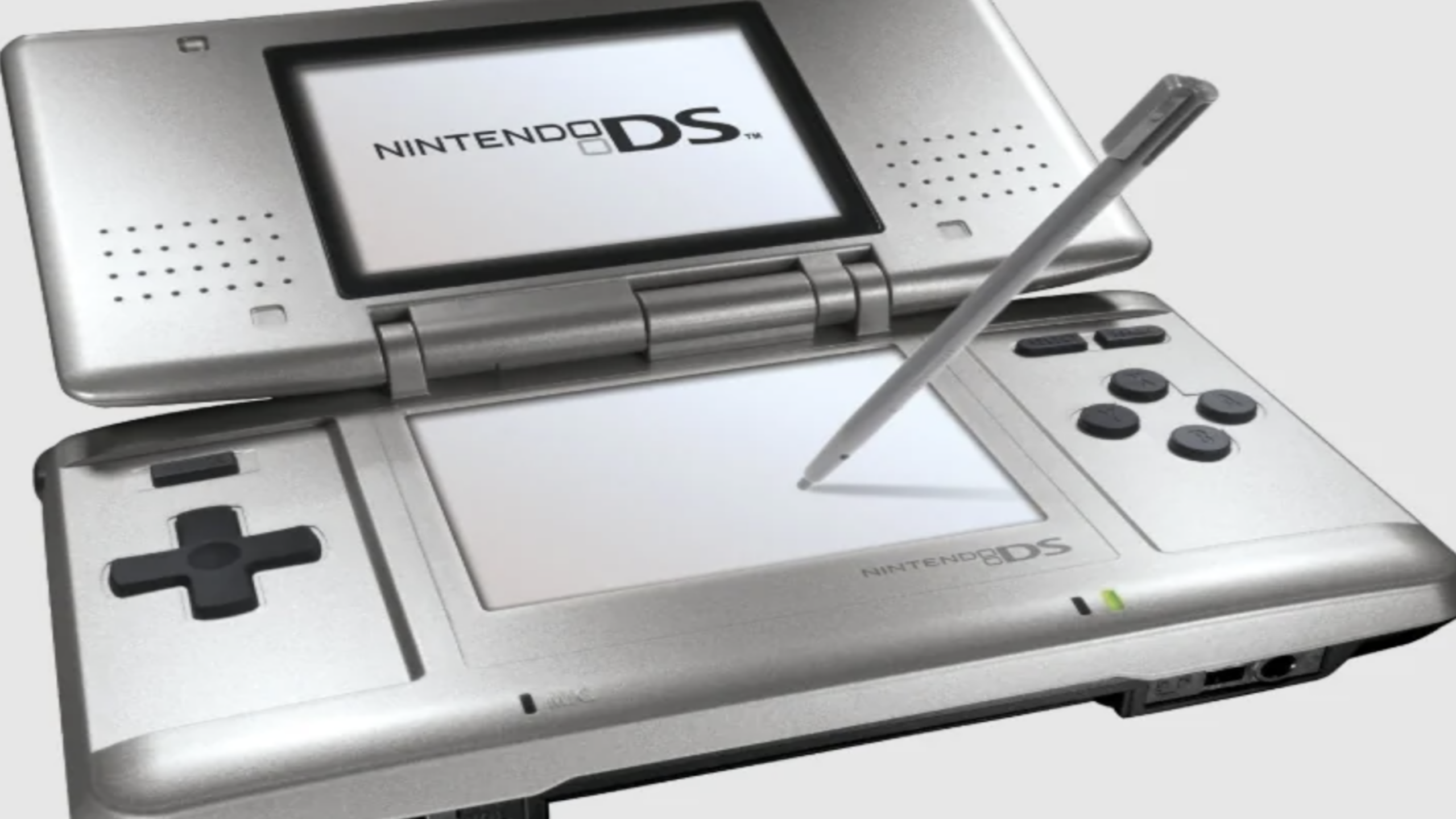 A silver Nintendo DS handheld console, part of the iconic line of Nintendo consoles, is open and displaying its logo on the top screen. A stylus is pointed at the blank lower touchscreen, with control buttons visible on the right and left sides.