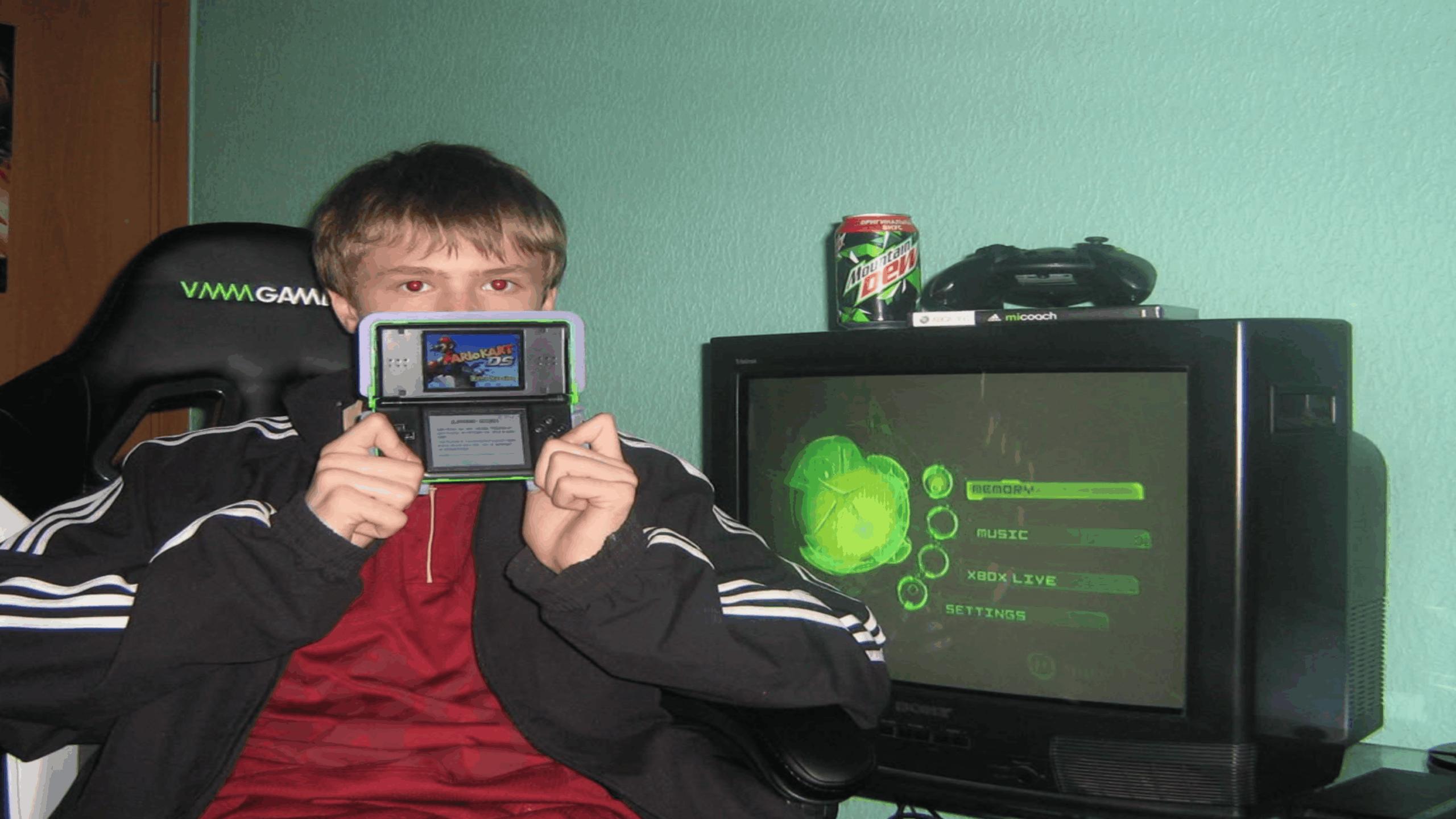 A person in a red jacket holds a handheld game console, sitting beside a TV displaying a green menu. Showcasing their love for consoles, they have both a game controller and a Mountain Dew can resting on top of the TV.