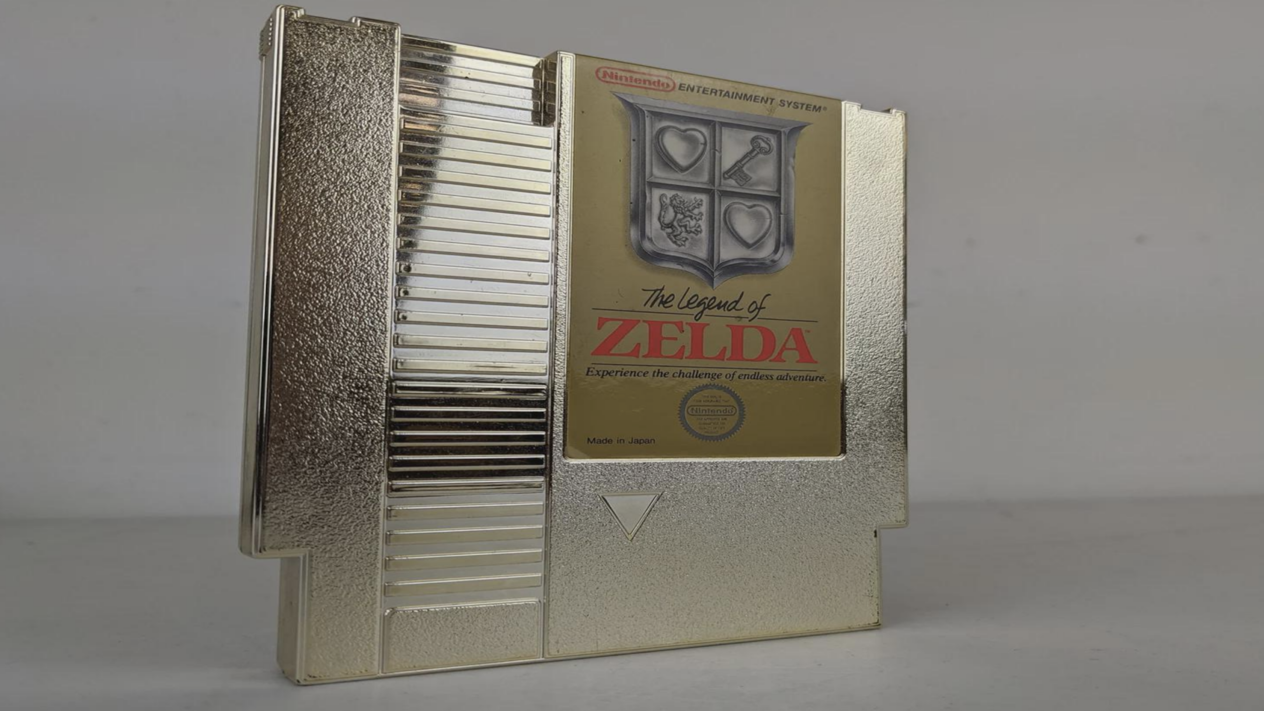 A gold Nintendo Entertainment System cartridge for “The Legend of Zelda” stands upright on a plain surface, displaying its iconic shield label and reflective finish—a timeless piece that marks the beginning of the legendary Zelda games.