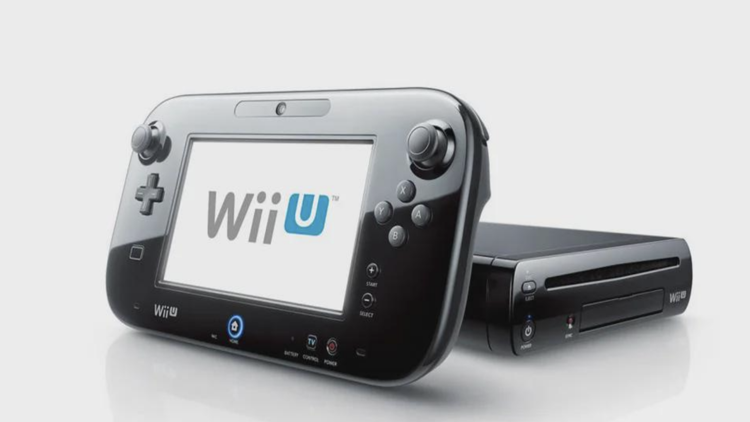 A Nintendo Wii U console, part of the celebrated family of Nintendo consoles, sits next to its gamepad controller, which displays the "Wii U" logo on its touchscreen. Both devices are black and shown against a white background.