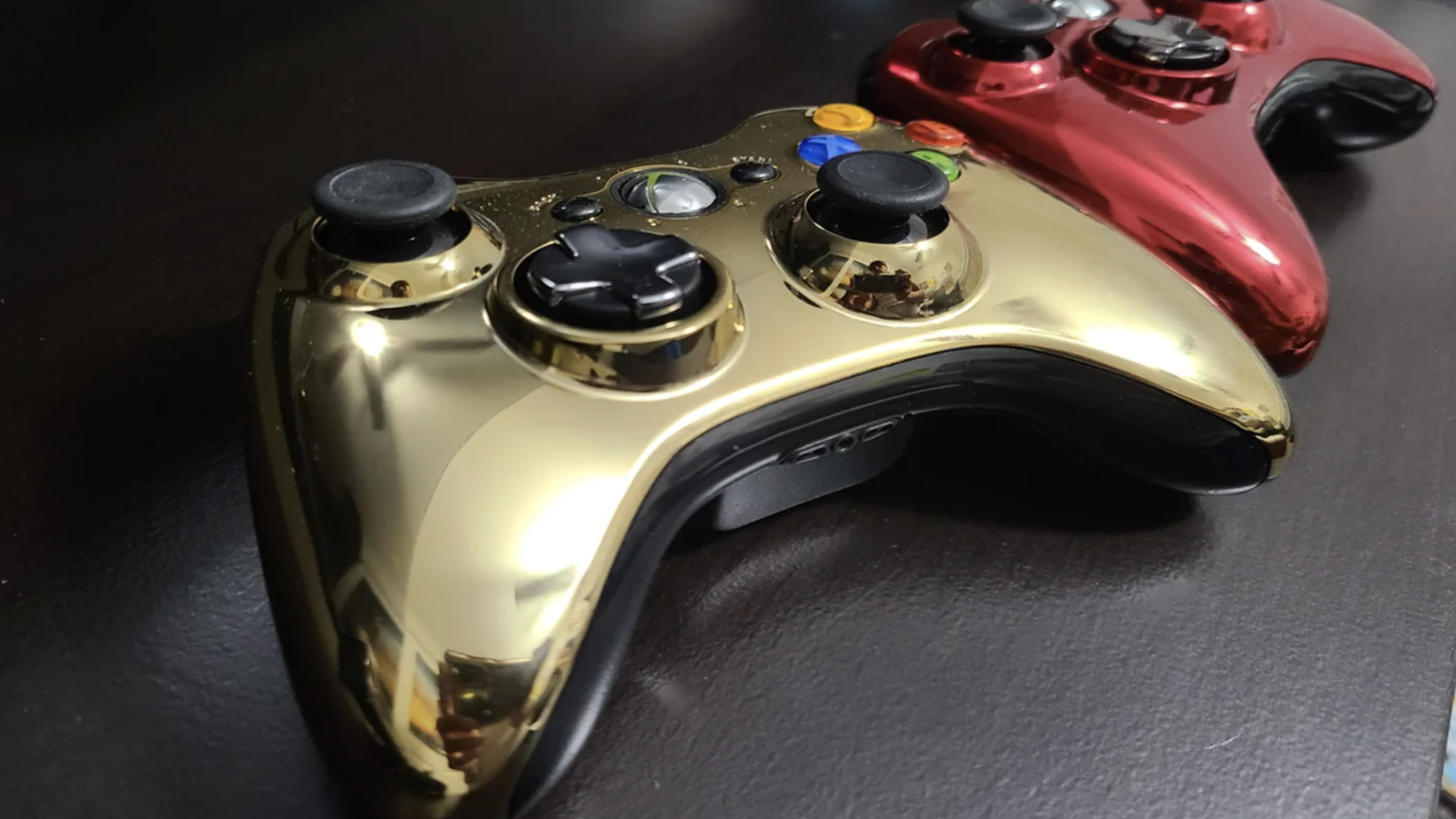 Two glossy Xbox 360 controllers sit on a dark surface, showcasing an air of expensive gaming, with one featuring a gold finish in the front and the other displaying a red finish in the back.