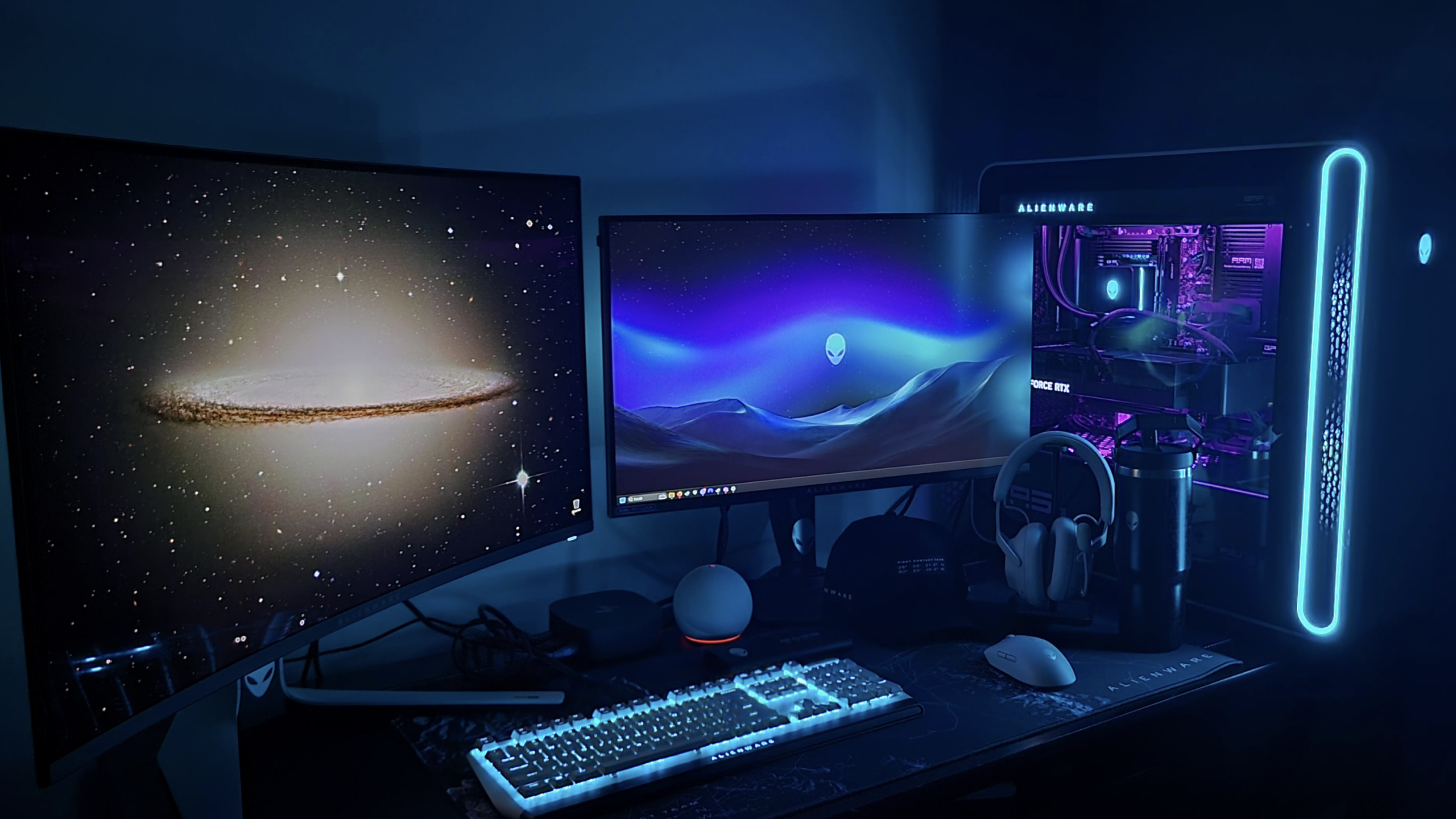 Dual-monitor gaming setup featuring top-tier Gaming Products: a glowing PC tower, RGB-lit keyboard, headphones on a stand, mouse, and space-themed wallpapers—all in a dim room bathed in blue and purple lighting.