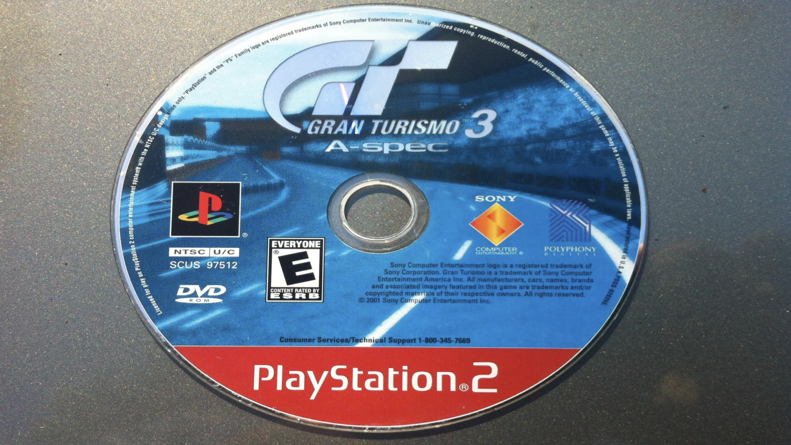 A PlayStation 2 Game Disc for “Gran Turismo 3 A-spec,” featuring the game’s logo, an image of a racetrack, PlayStation 2 branding, and the ESRB rating “E for Everyone.” This collectible Game Disc is perfect for racing fans and PS2 collectors alike.