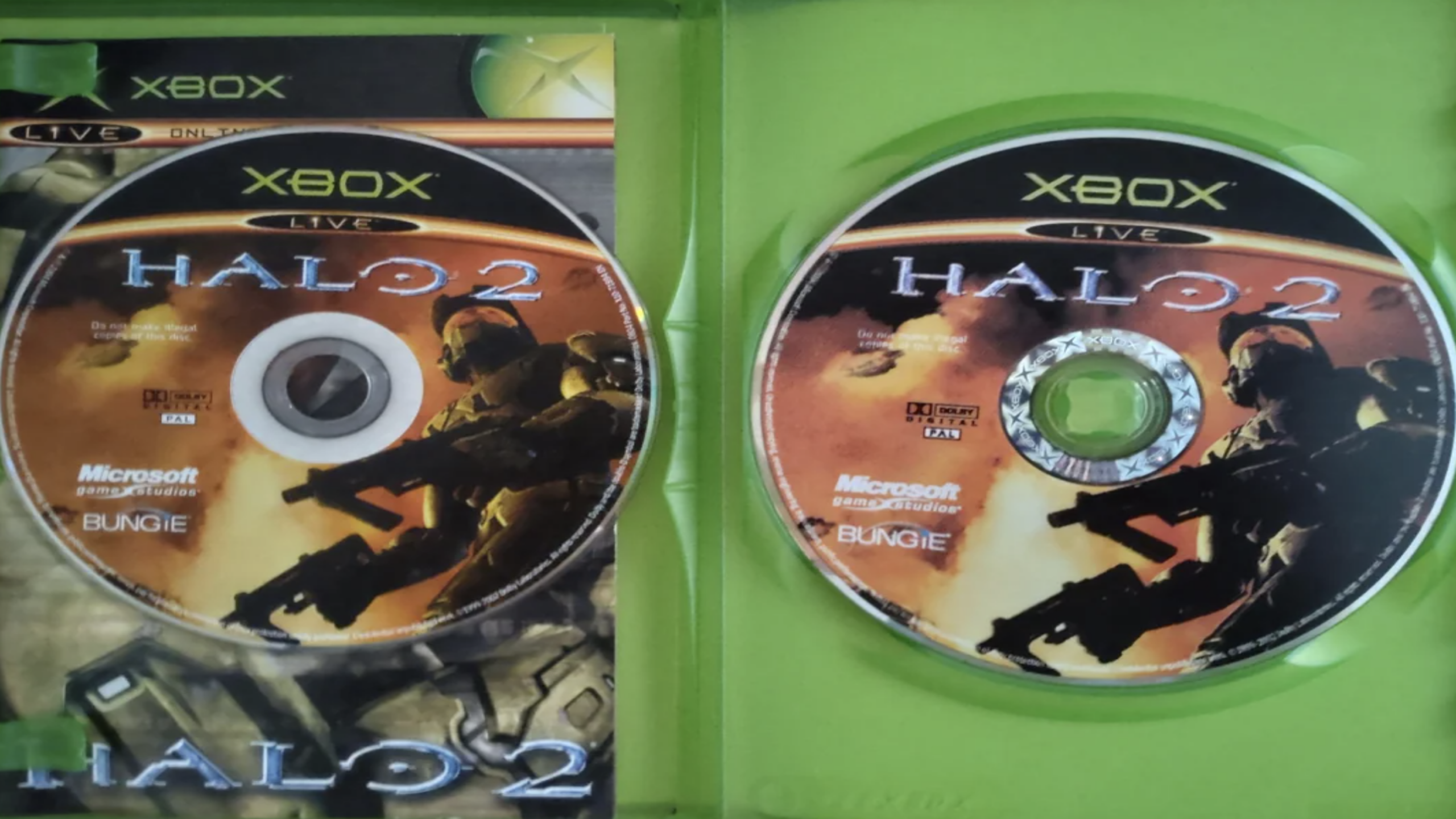 Two “Halo 2” Game Discs nestled inside a green Xbox game case, featuring striking artwork of armored soldiers and the prominent Microsoft and Bungie logos visible on each disc.
