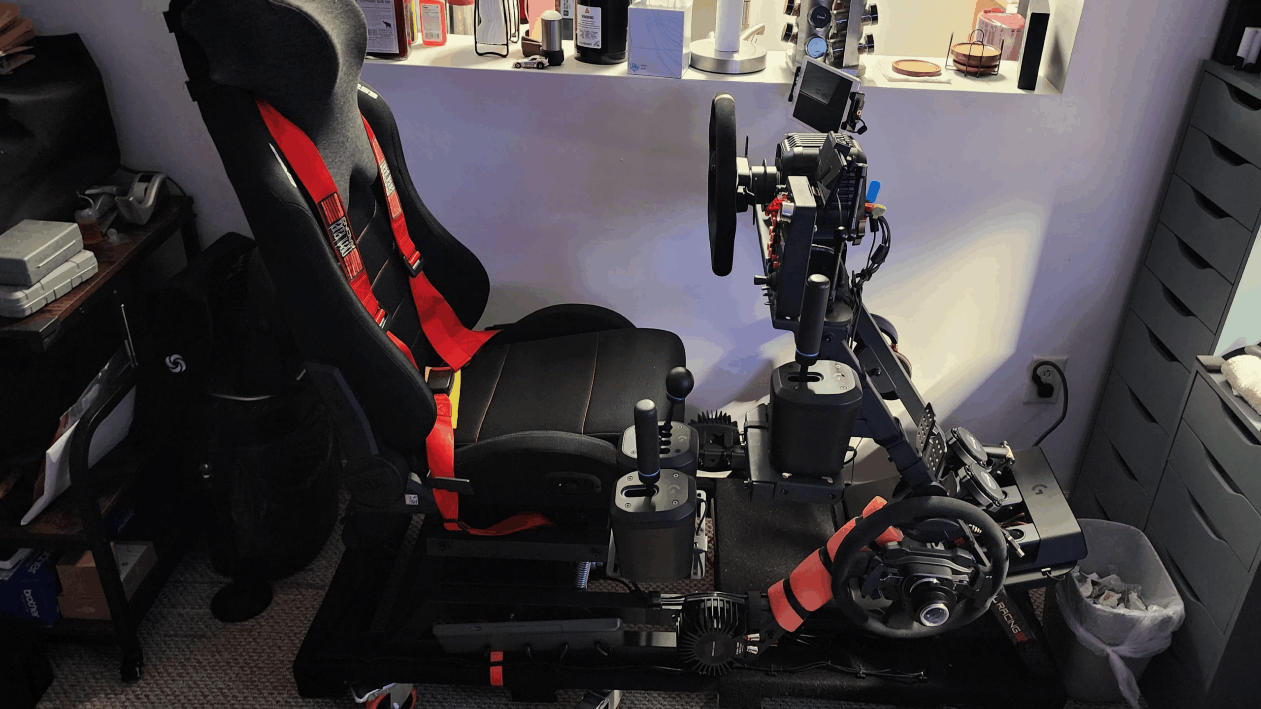 A racing simulator setup featuring a black seat, steering wheel, pedals, gear shifters, and various controls—showcasing top-tier gaming products—is positioned in a room with shelves and drawers in the background.