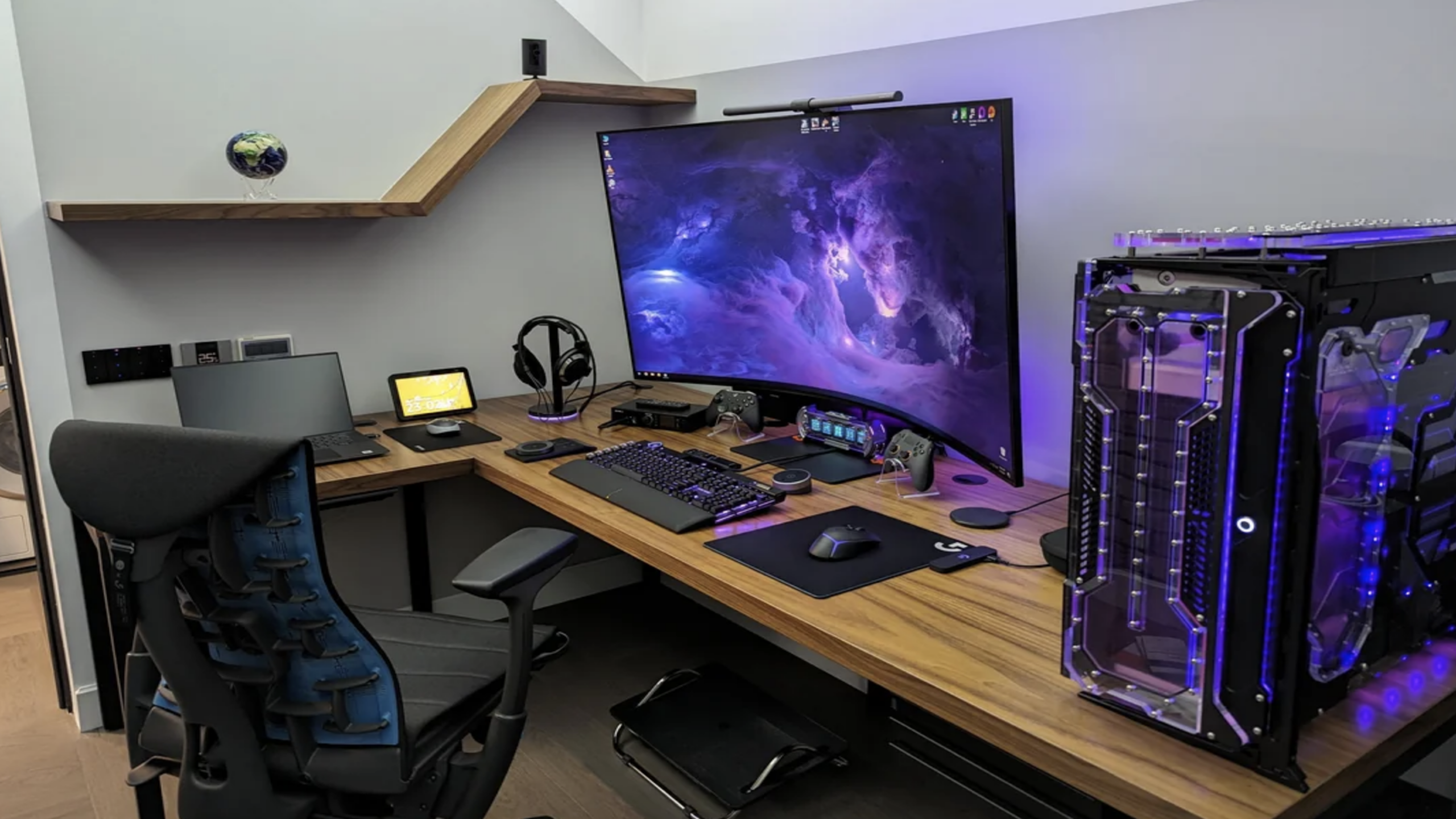 A modern gaming setup featuring top-tier Gaming Products, including a large curved monitor displaying a space scene, a gaming PC with vibrant purple lighting, sleek keyboard, mouse, headphones, controllers, small tablet, and an ergonomic chair arranged on a stylish wooden desk.