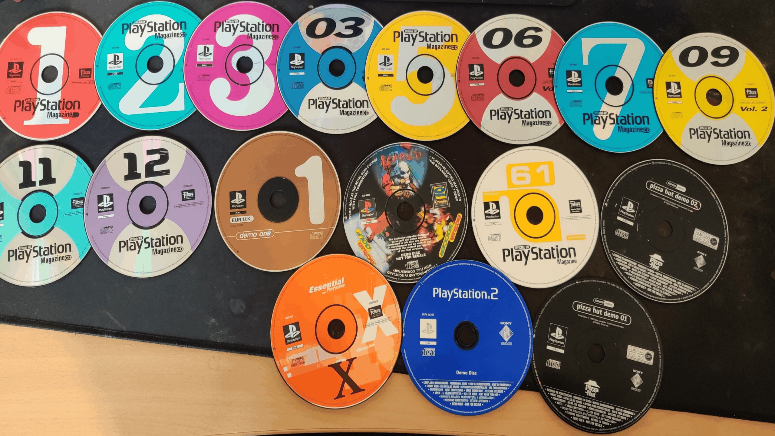 A collection of 17 PlayStation game discs, mostly numbered demo editions, arranged in two rows on a black surface. The colorful game discs feature titles from both PlayStation and PlayStation 2.