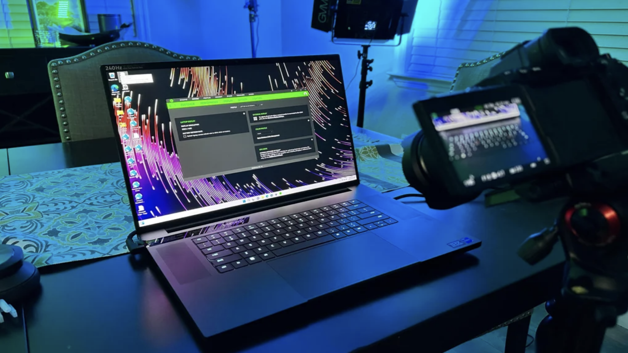 A laptop on a table displays colorful lines on its screen beside a digital camera on a tripod, with blue ambient lighting in the background—creating an atmosphere that’s perfect for showcasing the latest gaming products.