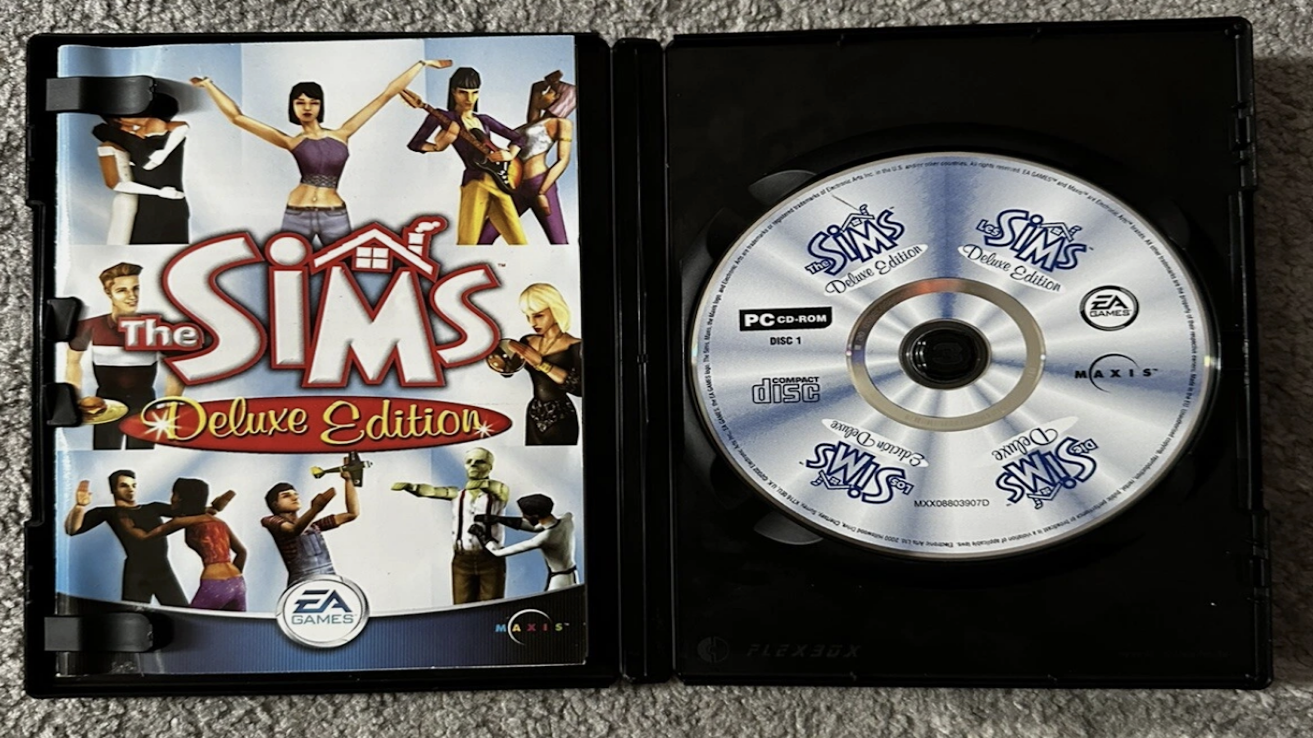 Open case of The Sims Deluxe Edition for PC, displaying the game cover with various Sims characters on the left and the Game Discs securely held in place on the right. Both feature branding from EA Games and Maxis.