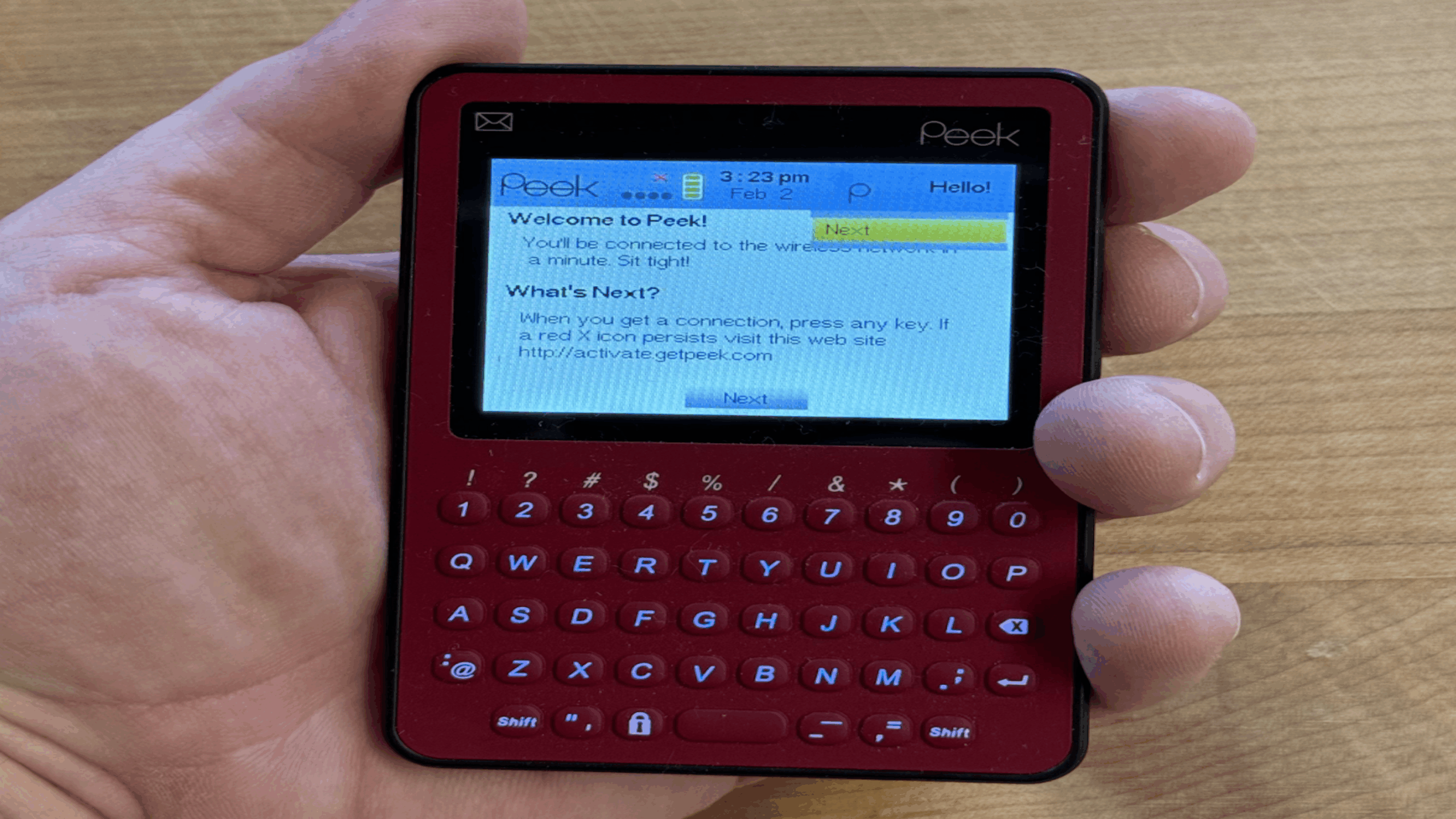 A hand holds a small red Peek device, one of the innovative tech gadgets featuring a QWERTY keyboard and a screen displaying a welcome message for web email setup.