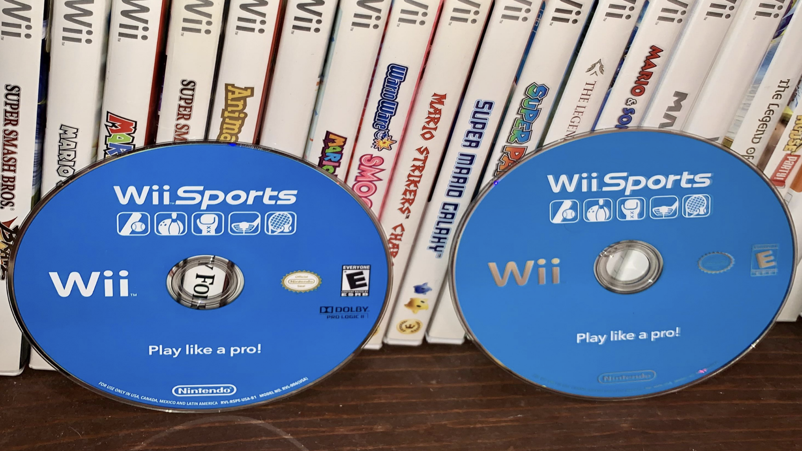 Two blue Wii Sports game discs are displayed in front of a row of Nintendo Wii game cases, including titles like Super Smash Bros., Mario Kart, and Animal Crossing. These game discs add a vibrant touch to any collection.