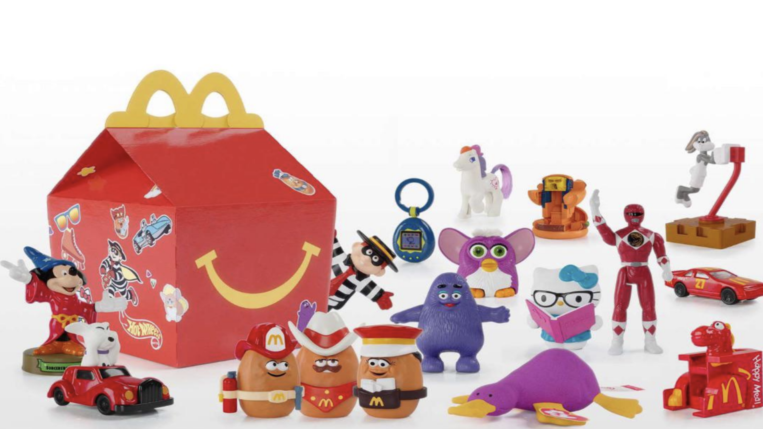 A McDonald’s Happy Meal box surrounded by various colorful childhood items, including cartoon characters, cars, action figures, and animals, all arranged on a white background.