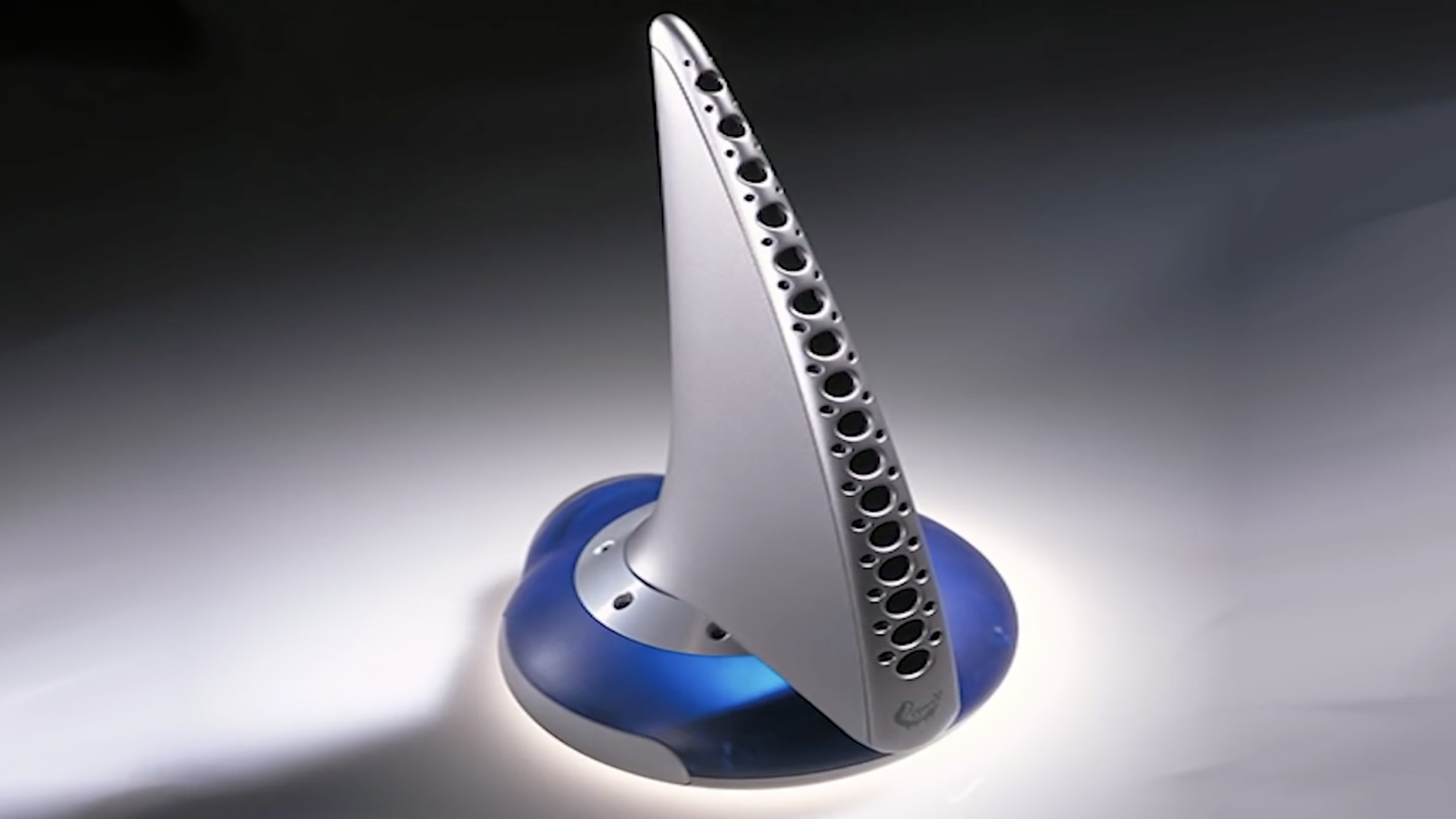 A futuristic, silver and blue vertical computer mouse with a base, featuring multiple holes along its curved surface, displayed on a softly lit background—a striking addition to any collection of innovative tech gadgets.