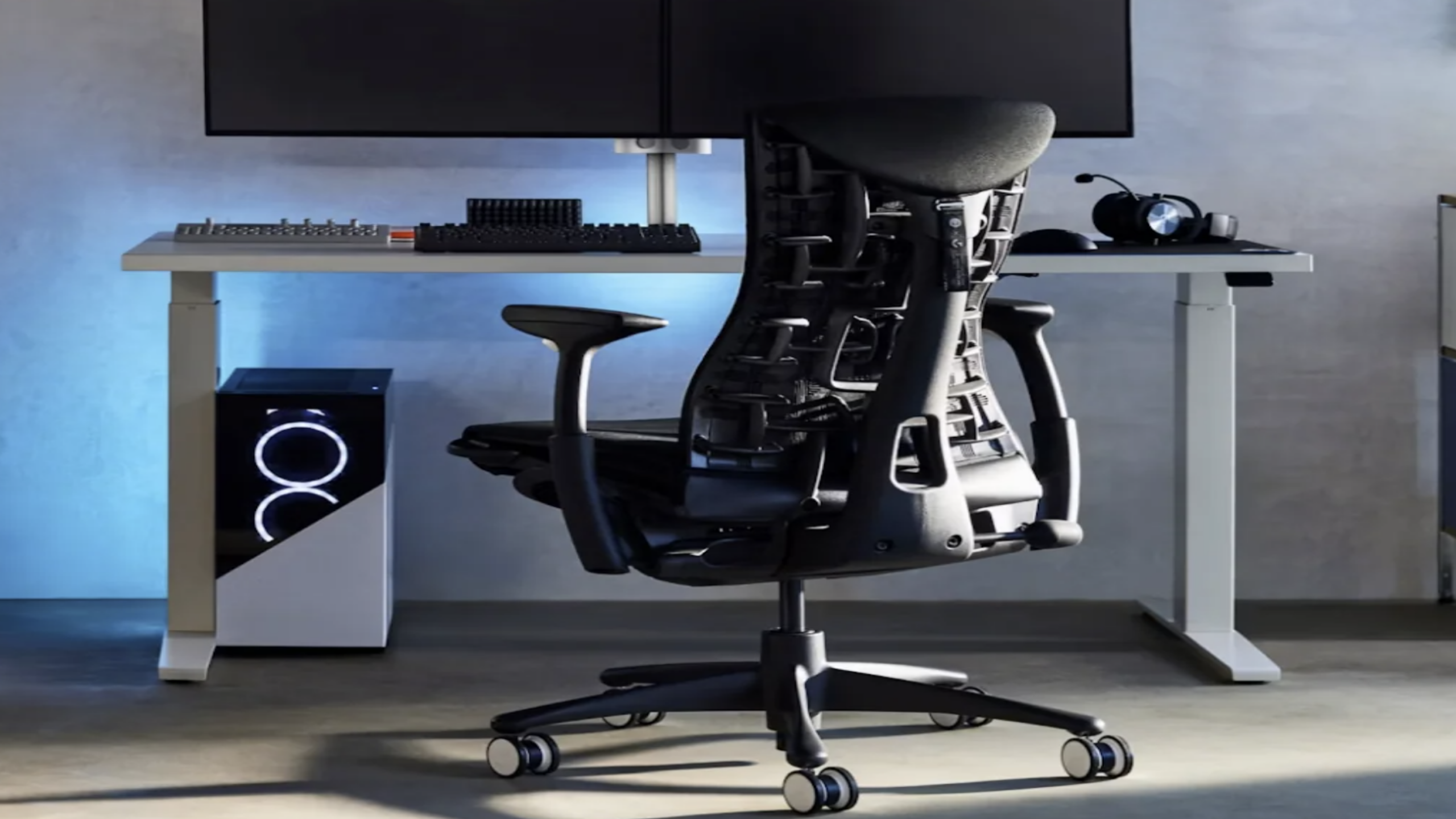 Ergonomic office chair at a modern desk setup with dual monitors, keyboard, and a sleek PC tower with glowing lights—featuring top-tier gaming products—all illuminated by soft blue ambient lighting.